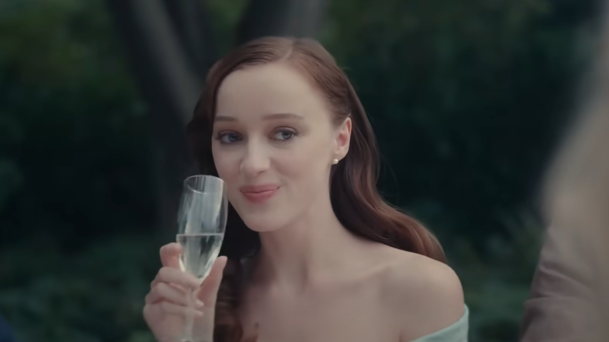 Scene from Anniversary movie 2025 featuring a woman with long brown hair holding a champagne glass and smiling during an outdoor celebration. The Anniversary movie captures moments of suspense, emotion, and family drama with a stellar cast including Phoebe Dynevor and Diane Lane.