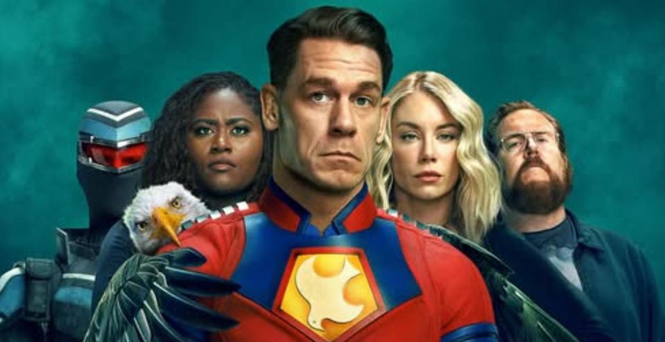 The main cast of Peacemaker Season 3 featuring John Cena as Peacemaker standing at the center in his red and blue costume, with his team Vigilante, Adebayo, Harcourt, and Economos in the background, along with his pet eagle, Eagly. The image has a teal-toned backdrop and represents the upcoming Peacemaker Season 3 series.